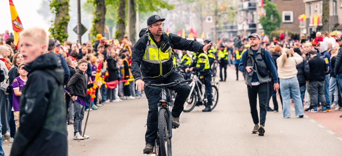 Security guard cycling beside a long queue of people.