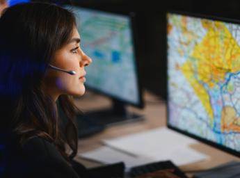 Female professional working in an alarm control center with a headset, monitoring a detailed map on a computer screen.