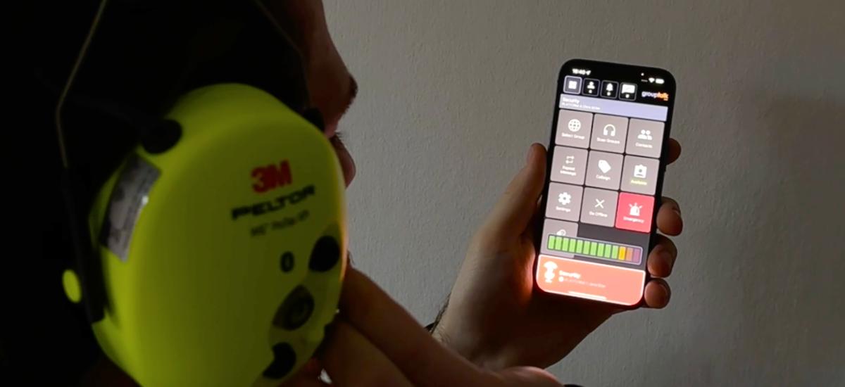Man using GroupTalk PTT app on iPhone with 3M Peltor headset.