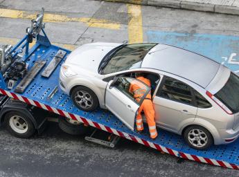 Roadside assistance worker securing car on tow truck after breakdown.