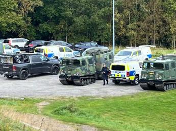 Police and military vehicles are parked together in a large field.