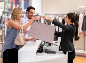Store employee giving a shopping bag to customer at checkout.