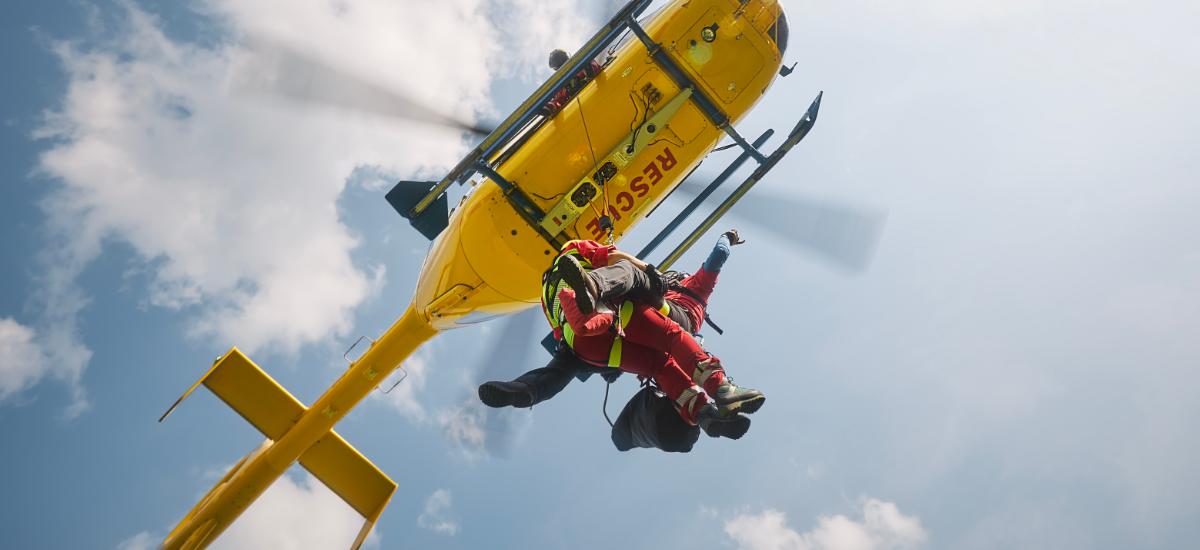 Rescue worker rappelling from helicopter on rope.
