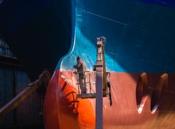 Workers painting ship bottom in dry dock.